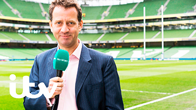 Broadcaster, Mark Pougtach in a rugby stadium.